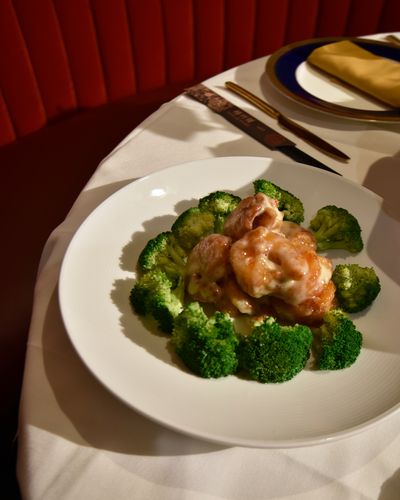Grand Marnier's prawns in a creamy glaze ringed with broccoli on a white plate at the edge of a set table, with a red velvet banquette behind