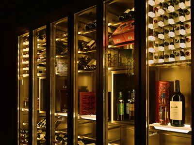 Backlit glass wine cabinets glowing gold, stocked with racks of wine and featured bottles of wine and spirits