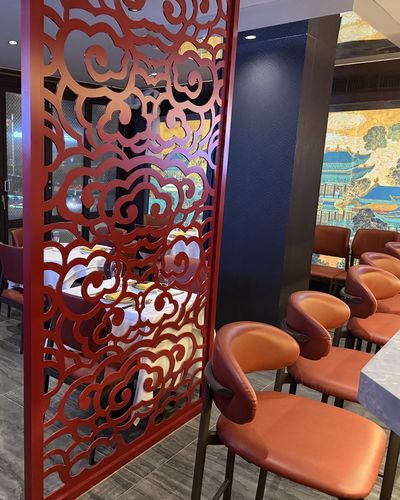 A red cloud-pattern carved screen between tables, with orange leather chairs and a section of the painted palace mural