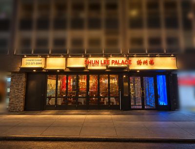 The Shun Lee Palace storefront at night beneath an office building, its long lit sign running across the facade.