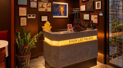 The host stand: a grey stone desk with a glowing gold “SHUN LEE PALACE” band, framed awards and a blue dragon painting on the wall behind.
