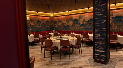 The main dining room: round tables set in white linen beneath a long hand-painted mural of pagodas and pine trees.