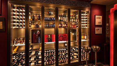 Backlit glass cabinets of wine and spirits on a deep red wall, with two stainless steel ice buckets.