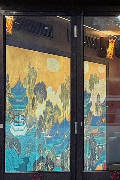 A painted palace mural seen through the restaurant’s glass front doors at night